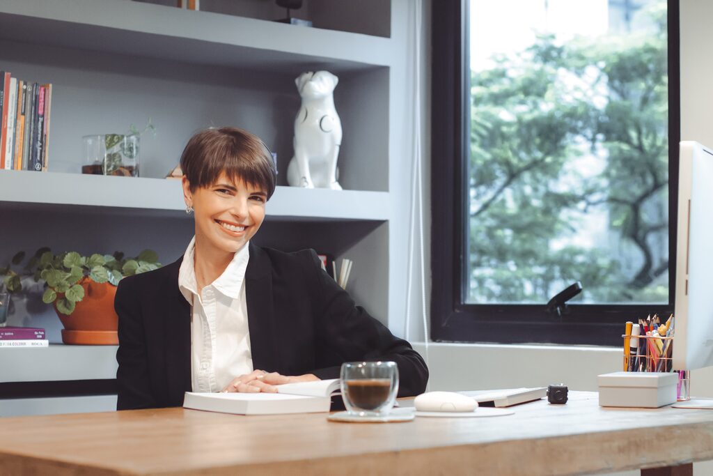 Danielle Rossini em sua mesa de trabalho, com estante de livros técnicos ao fundo.