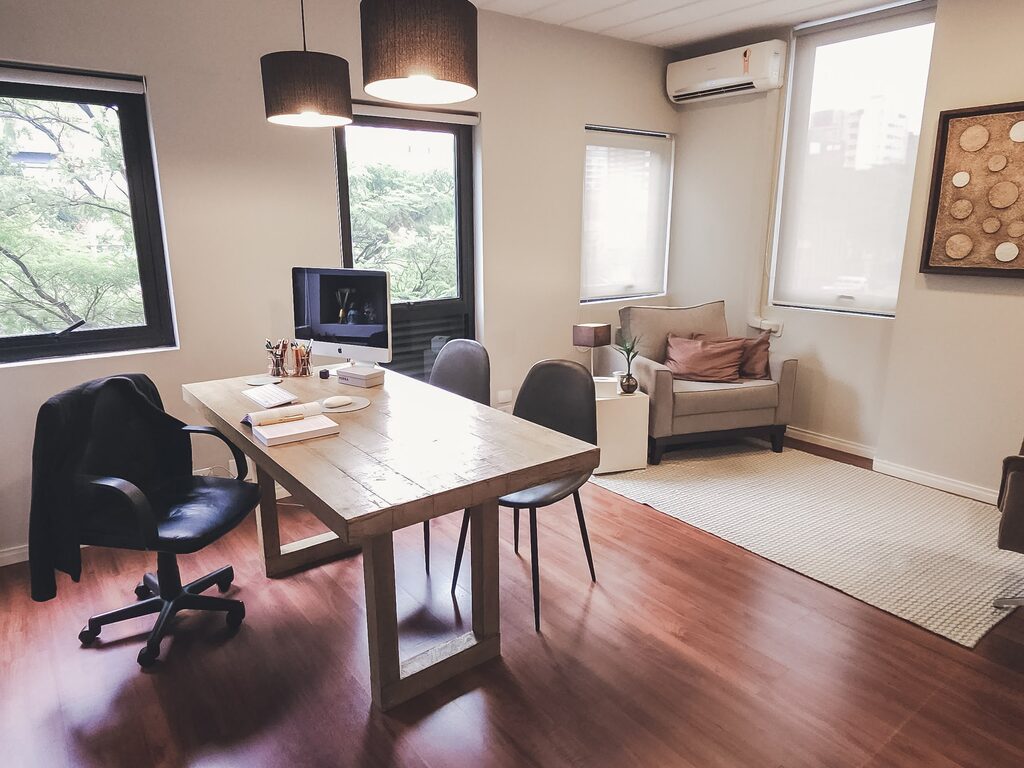 Sala de atendimento com mesa de madeira, poltronas e janelas amplas.