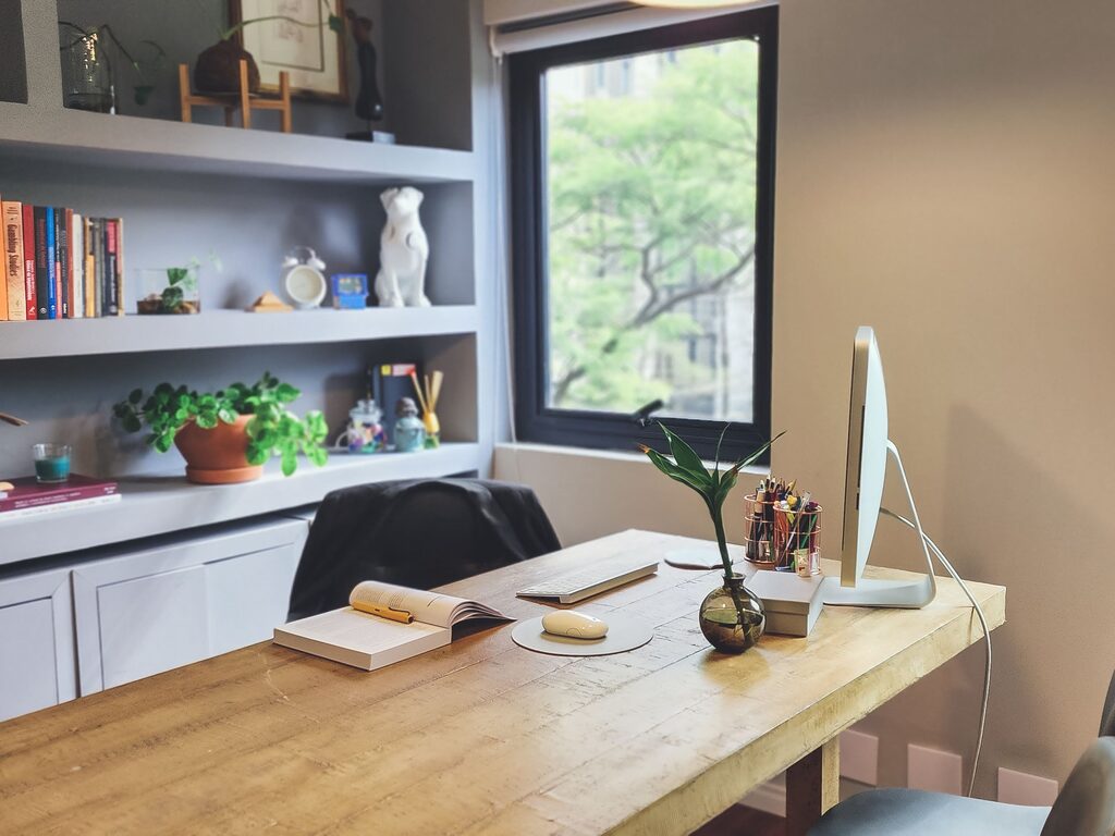 Mesa de trabalho de Danielle Rossini, com estante de livros técnicos ao fundo.